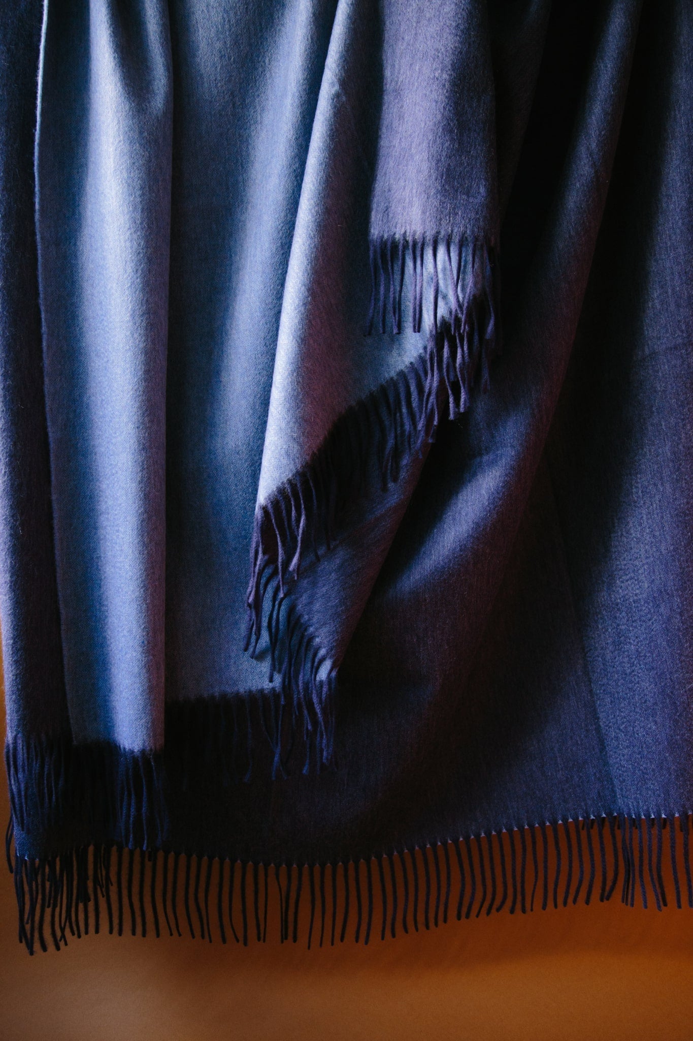ALT=Large cashmere throw. Two sided reversible colour; navy and denim blue. Draped against a brown background with natural light.