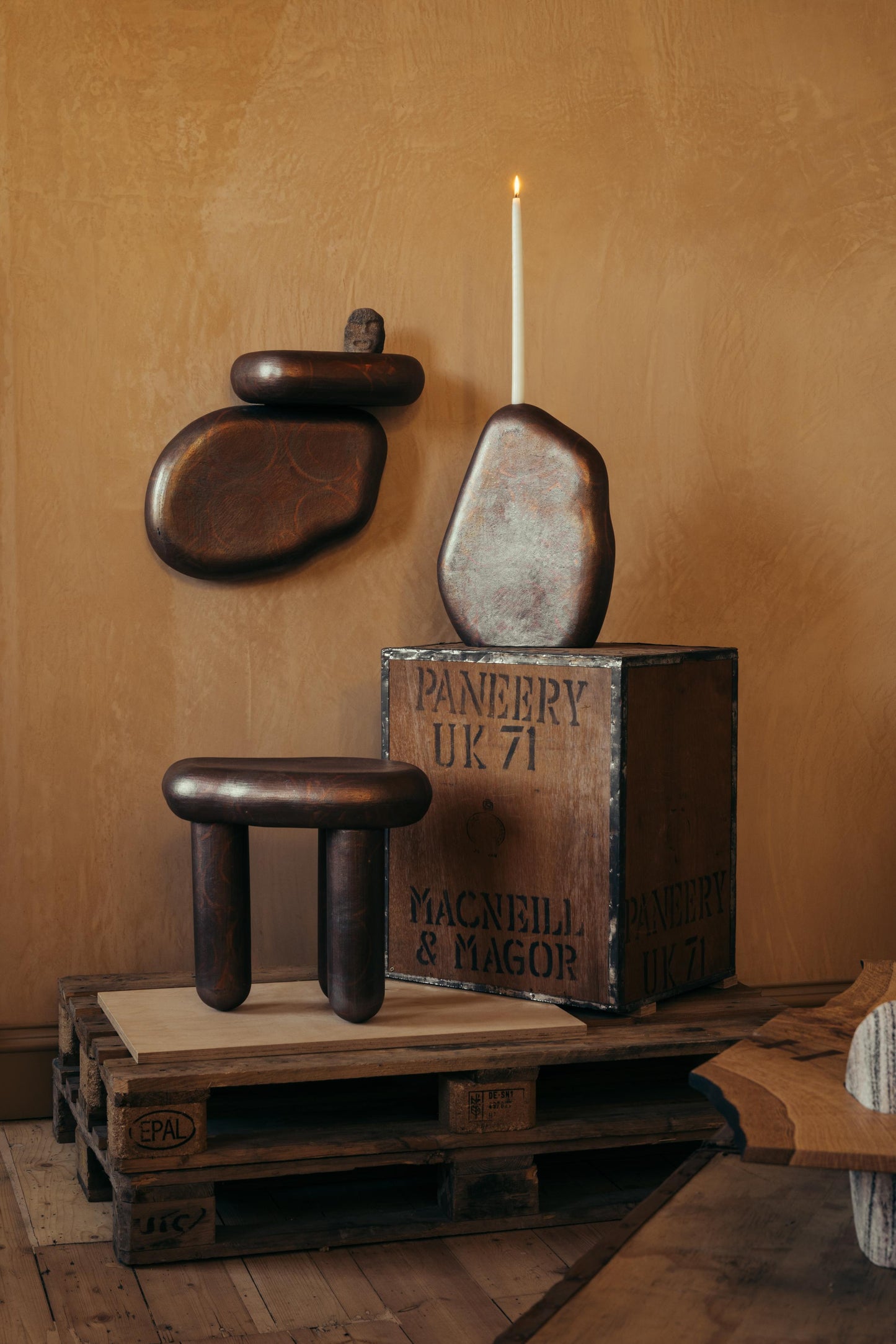 ALT= Ceramic Hermit Furniture by James Rigler. A three-legged table, candlestick, and shelf. In a deep bronze tone. Photographed at Bard Scotland, a gallery and shop in Leith, Edinburgh.