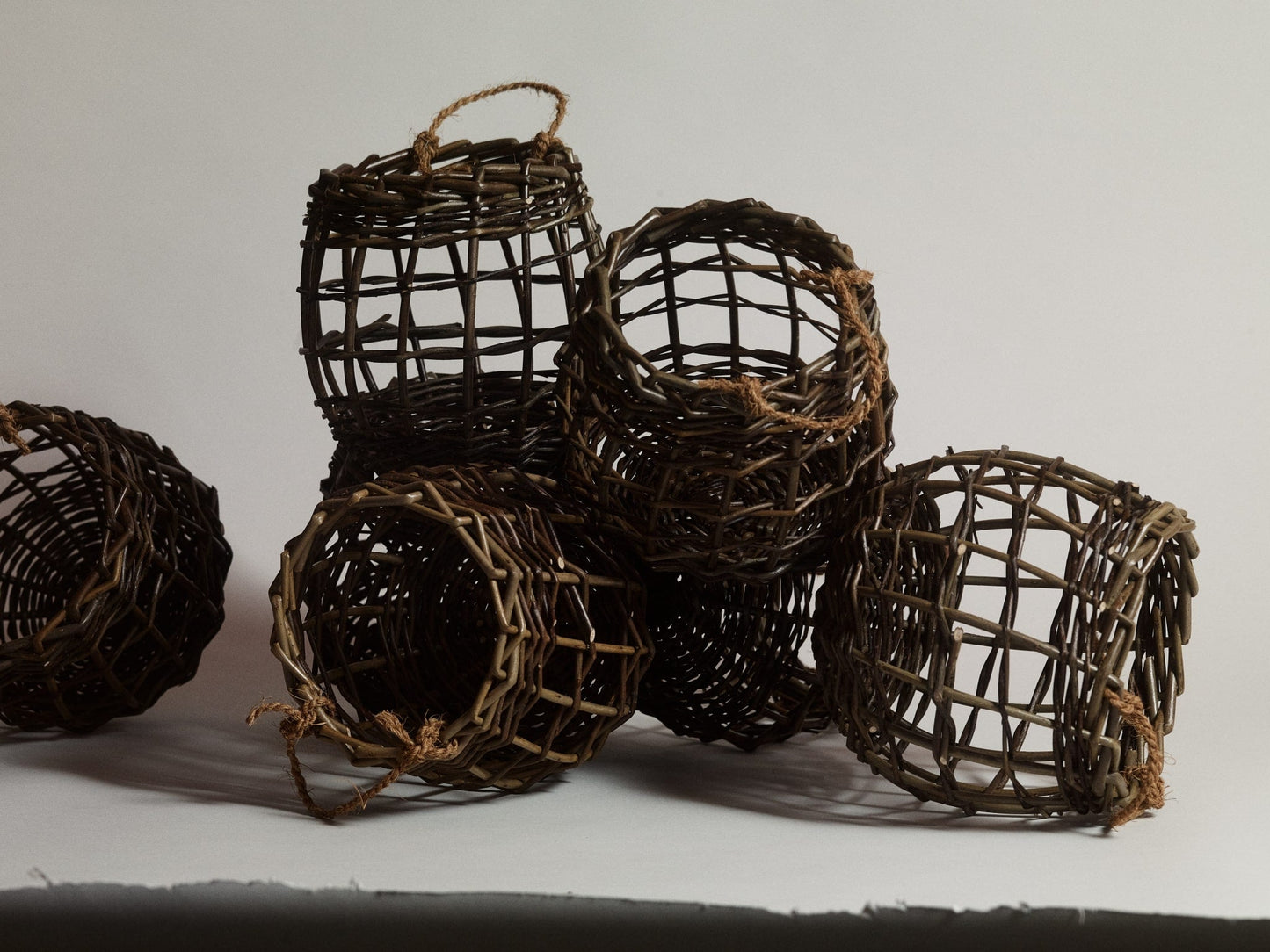 ALT=Small fruit and vegetable pots woven from willow with string handles. Six shown in frame, on a grey paper background.