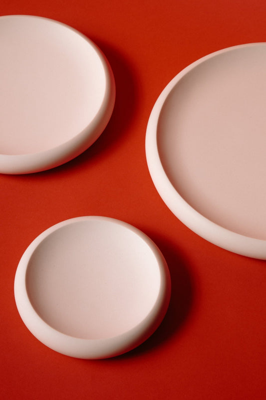ALT=Three white jesmonite plates on a red background. Stacked in size order, small, medium, and large.
