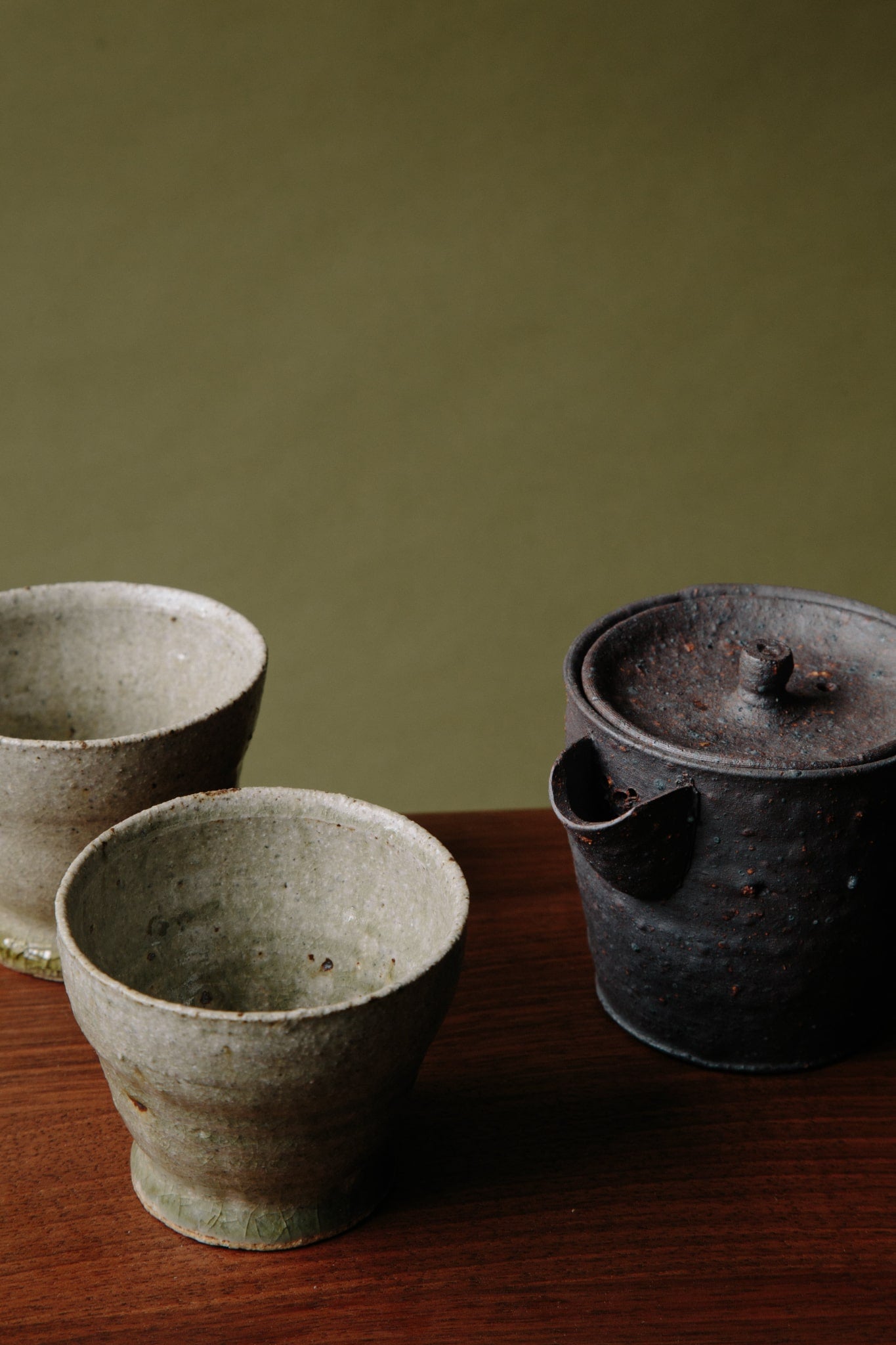 ALT=The small black teapot photographed with two ceramic cups with feet, also by Jonathan Wade.