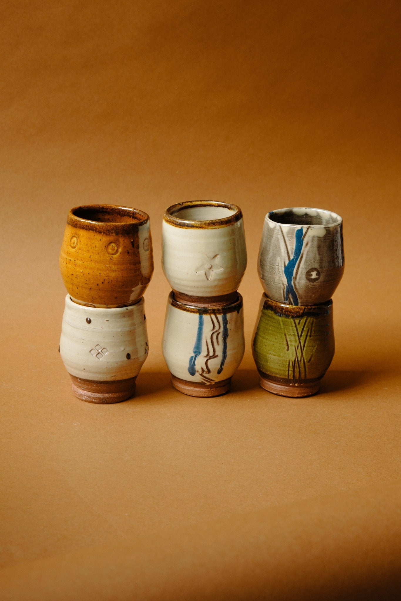 ALT=A set of six drinking vessels, two balanced on top of one another. In shades of white, green, caramel and blue,with a glossy finish and small foot.