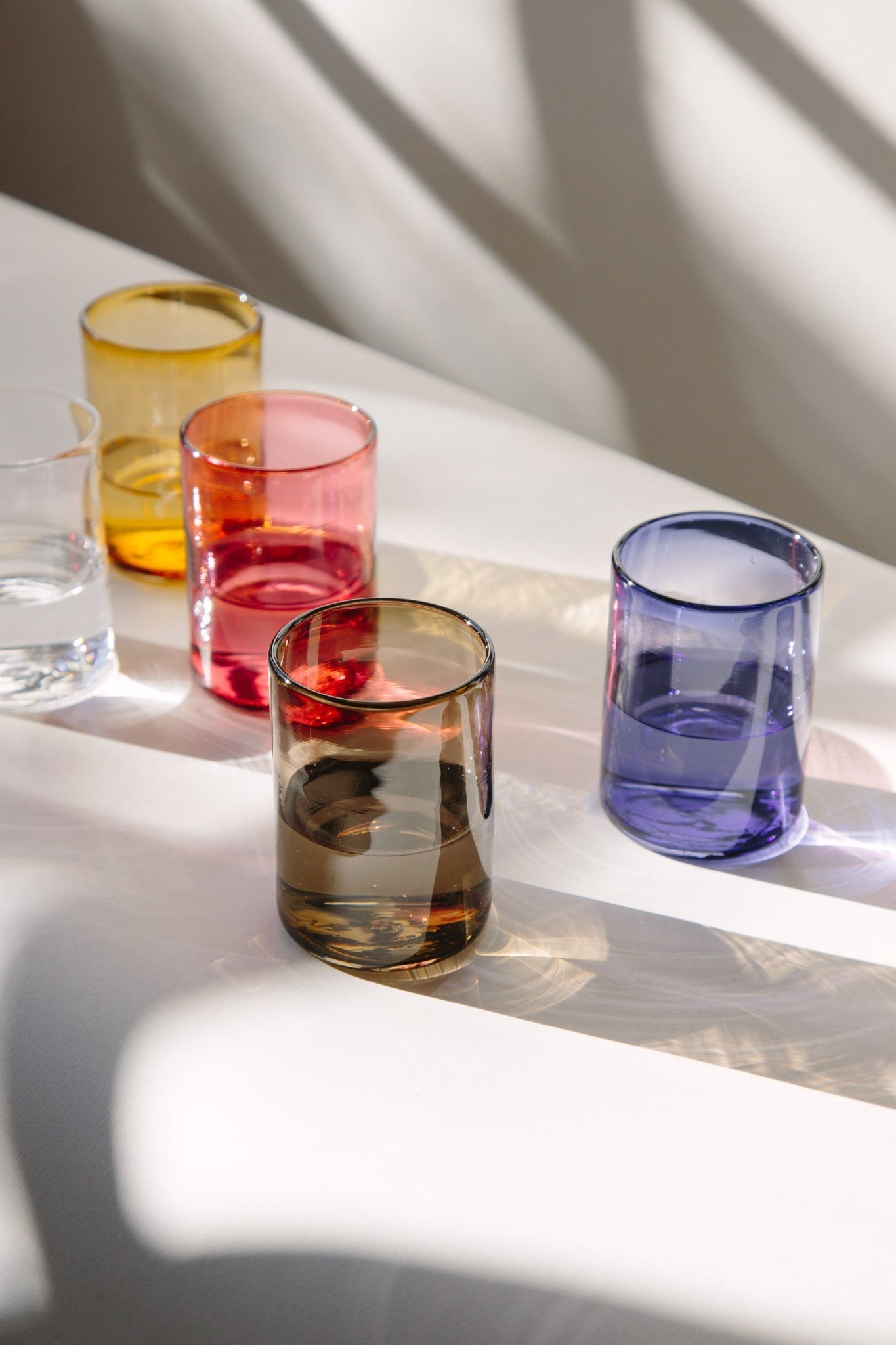 ALT=Five tumblers in hand blown glass. Natural light casting geometric shadows and reflections.