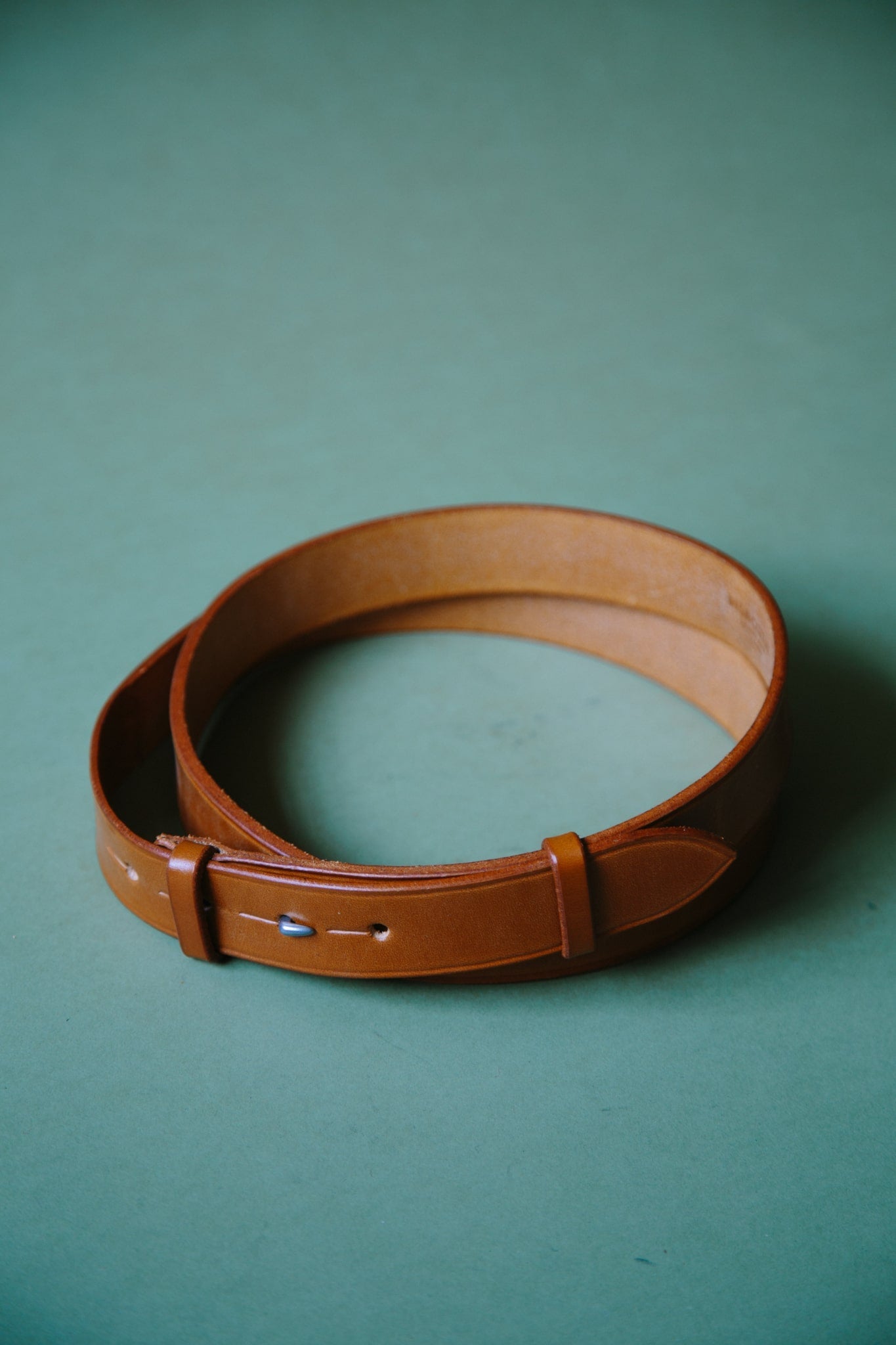 ALT=A tan bridle leather belt, wrapped into a circle so it fits within frame. The belt is buckleless and the hook and stud fastening can be seen.