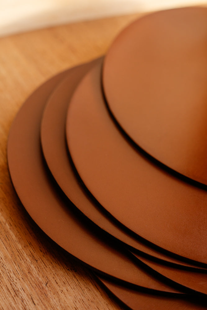 ALT=Close up shot of a stack of leather placemats from McRostie Leather placemats in tan. Shot at Bard Scotland, a shop and gallery in Leith.