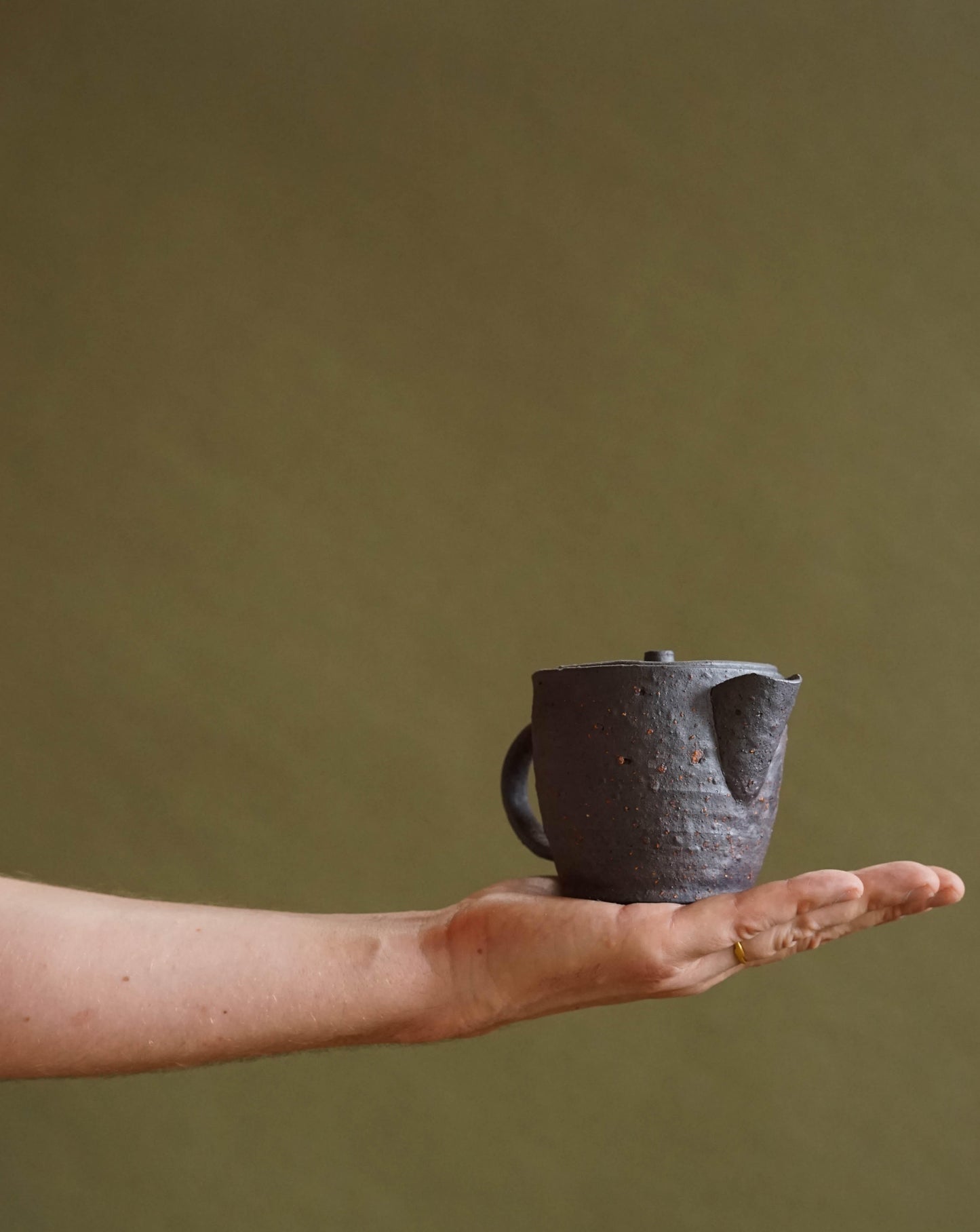 ALT=Hand holding the small black teapot by Ingot Objects.