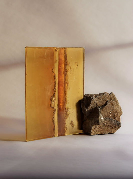 ALT= One of three works by Jack Brindley, named 'Prism for the shore'. Made of stone and pieces of coloured glass. This one shows an amber piece of glass, with mottles and purposeful fingerprints.