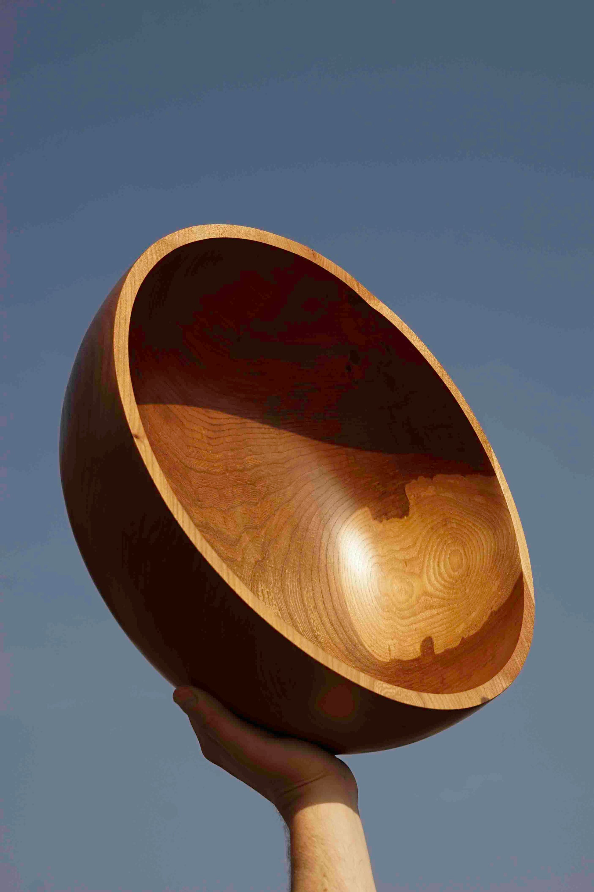 ALT=Jonnie Crawford's Wych Elm bowl. Held in the air by a hand from the bottom of the image. The inside of the bowl faces the sun.