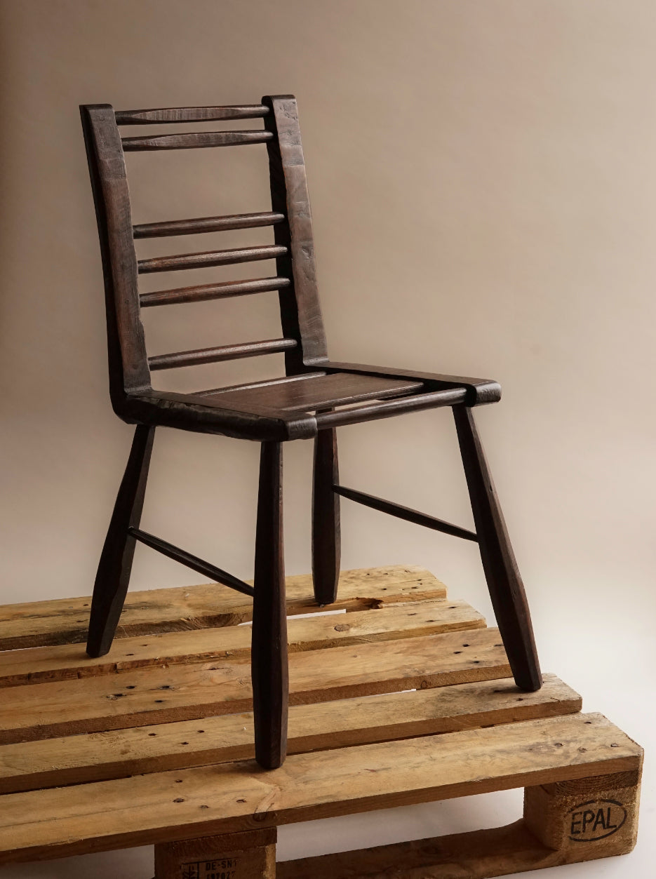 ALT= The Caithness Chair stands on top of a wooden palette. The chair back is made of six horrizontal narrow beams, and the seat is made of one larger flat piece of wood, and another two of the narrow beams.