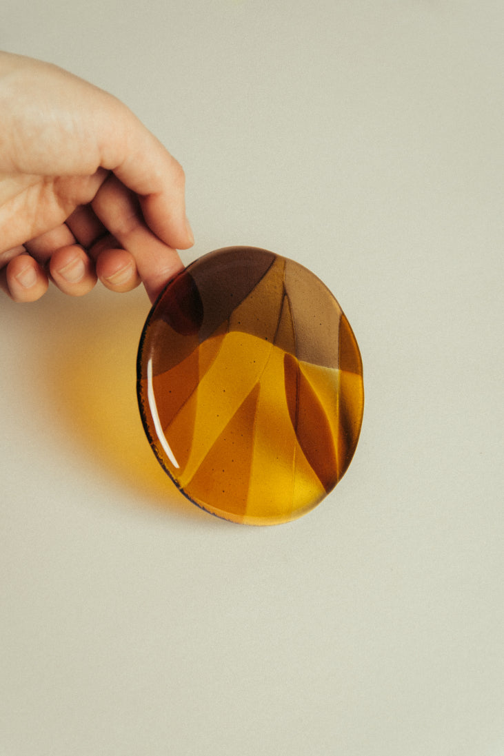 Hand holding a round amber glass coaster against a beige background