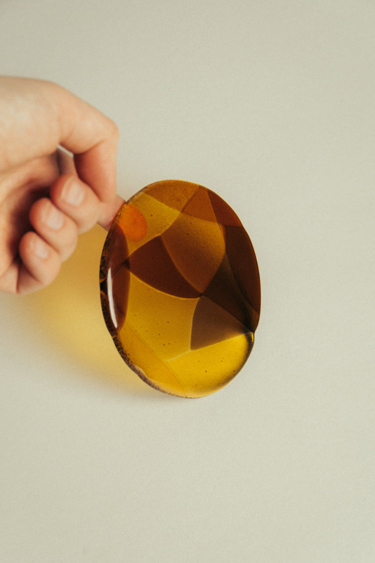 Hand holding a glass amber coaster against a neutral background