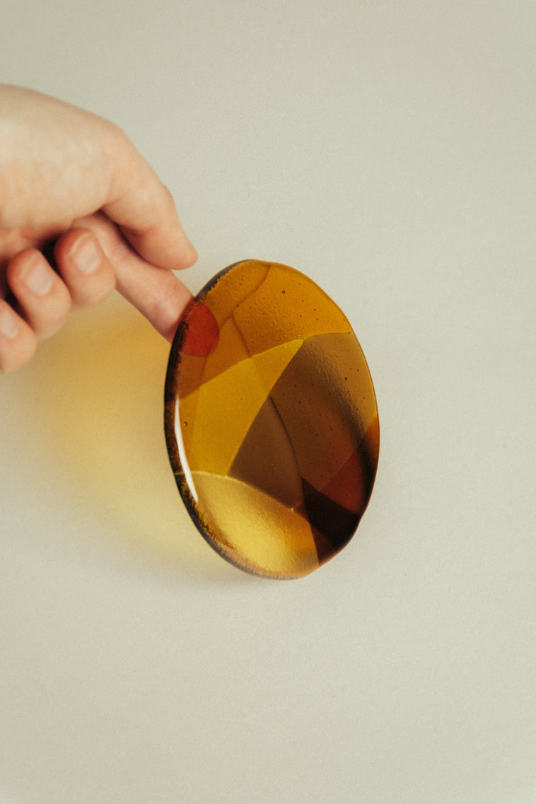 Hand holding a round amber glass coaster against plain background