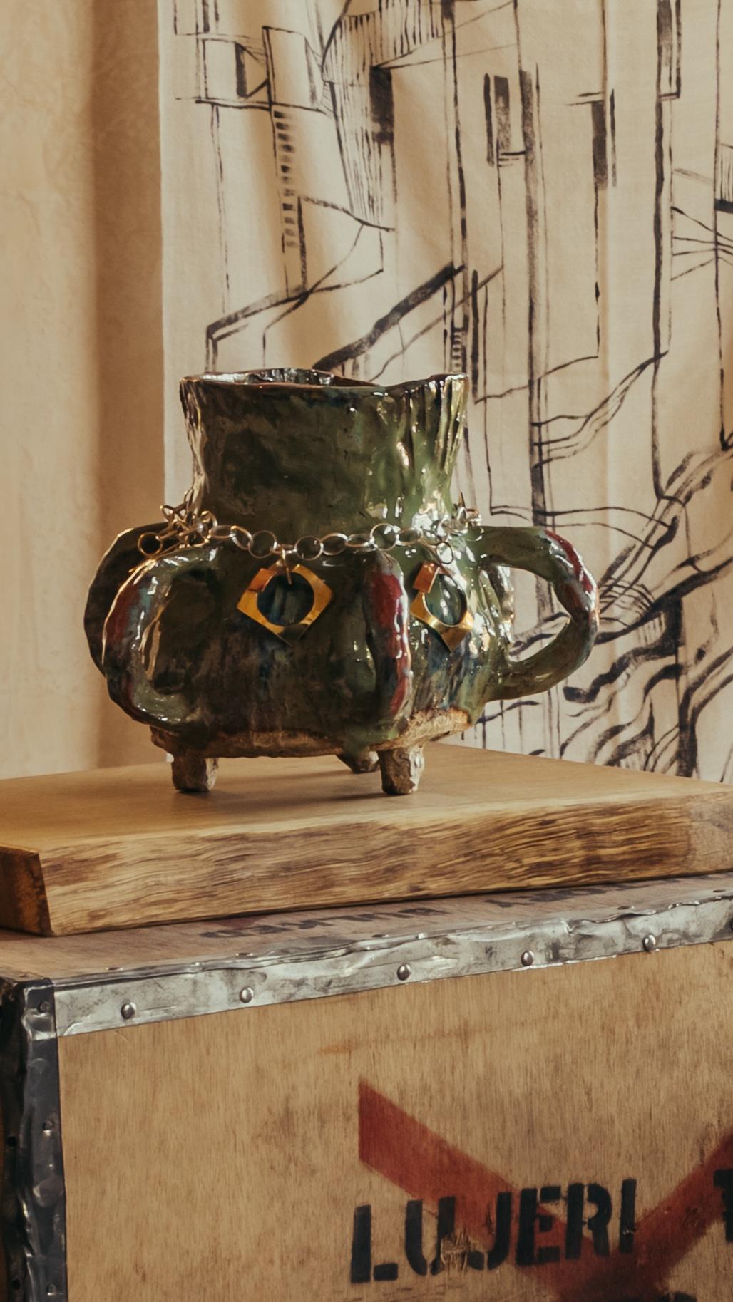 ALT= Ceramic vase with handles and feet by Glasgow based ceramicist and artist Morven Mulgrew. The vase sits on top of a wooden plank, and vintage tea box, as part of The Grit and The Glamour exhibition at Bard Scotland.