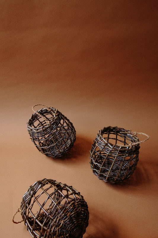 ALT=Small fruit and vegetable pots woven from willow with string handles. Three shown in frame, on a brown paper background. 
