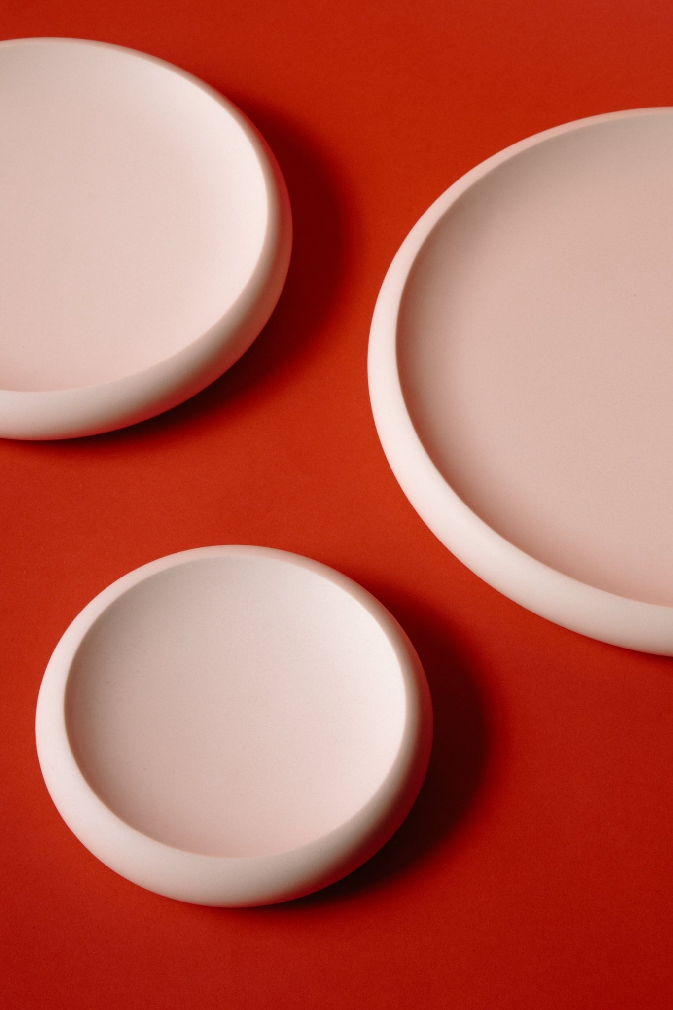 ALT=Three white jesmonite plates on a red background. Stacked in size order, small, medium, and large. 