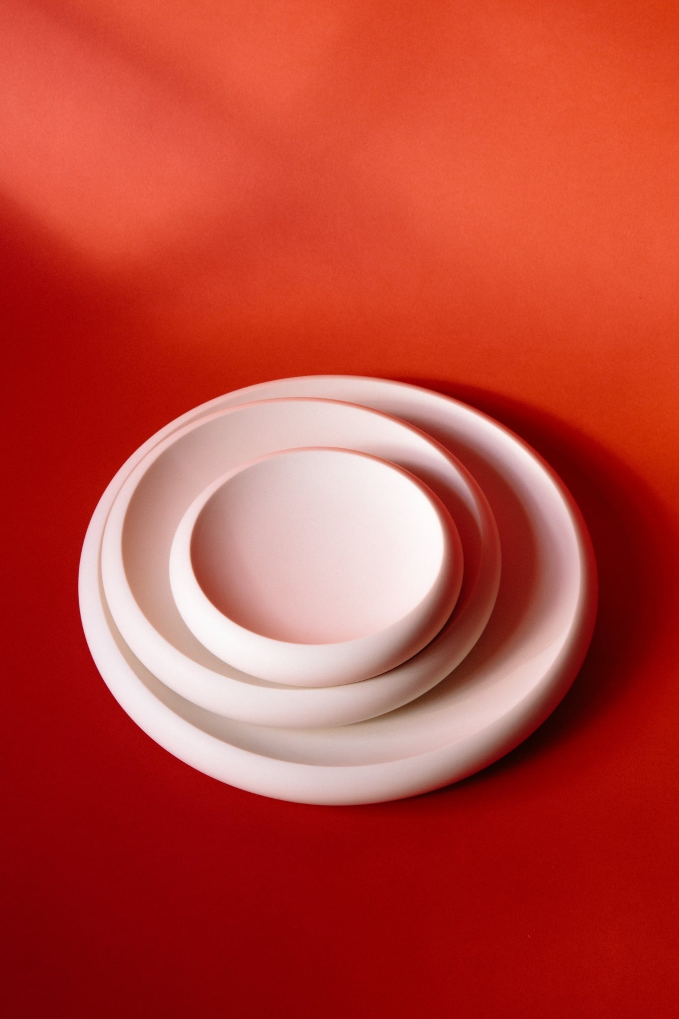 ALT=Three white jesmonite plates on a red background. A series of small, medium, and large versions, laid flat next to each other. 