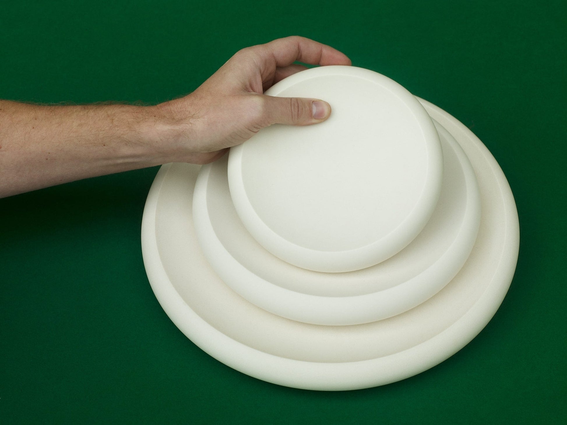 ALT=Three white jesmonite plates on a green background. The small being held by a hand coming in from the left, the medium and large lying flat.