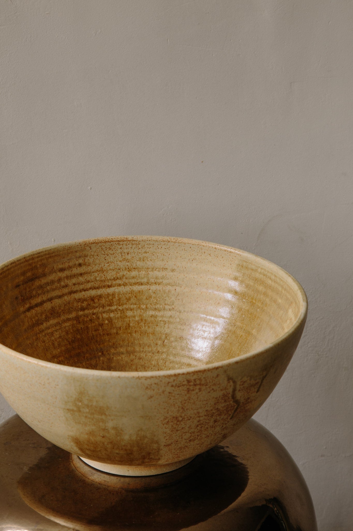 ALT=Large ochre yellow ceramic bowl placed on a metallic copper stool photographed in natural light coming in from the left.