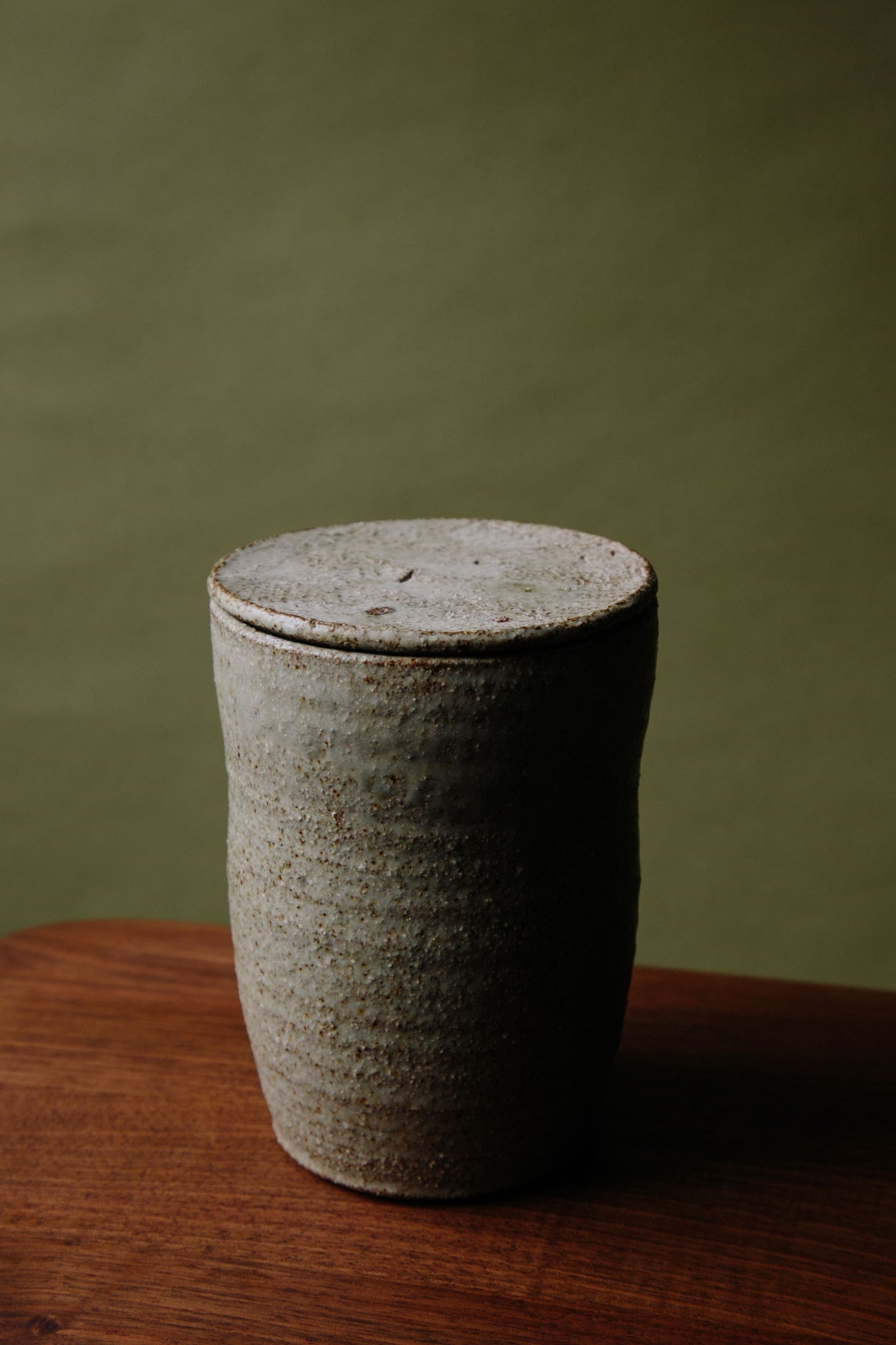 ALT=A third angle of the ceramic jar, this time with the lid on the jar. The concentric hand thrown lines can be seen and a dramatic shadow cast by the natural light coming in from the left.