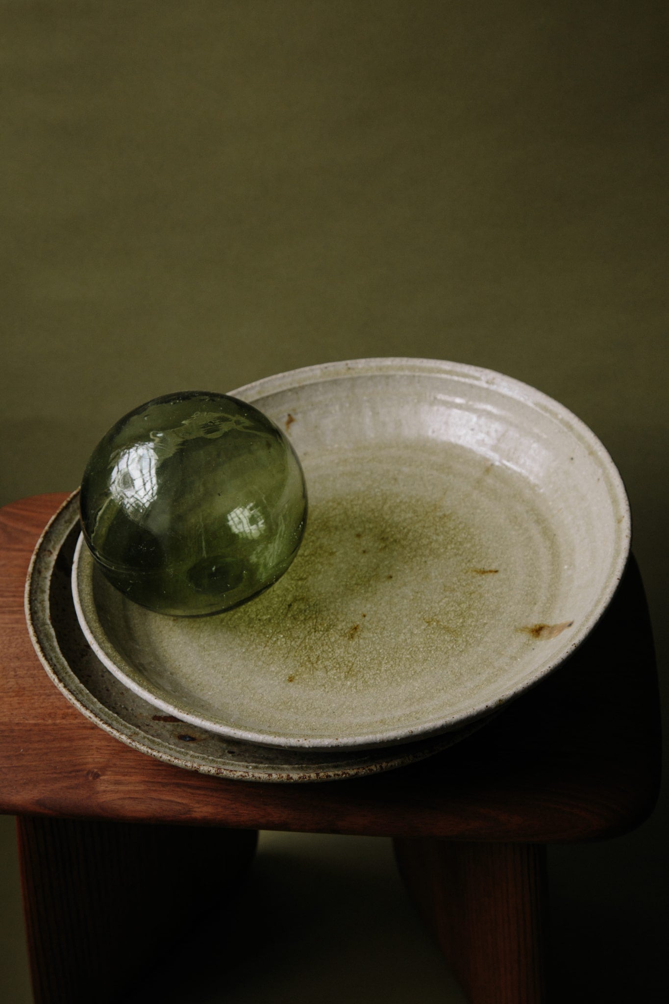 ALT=A stack of unique green ceramic platters with a green glass sphere balanced on the top platter. The glaze being reflected in natural light.