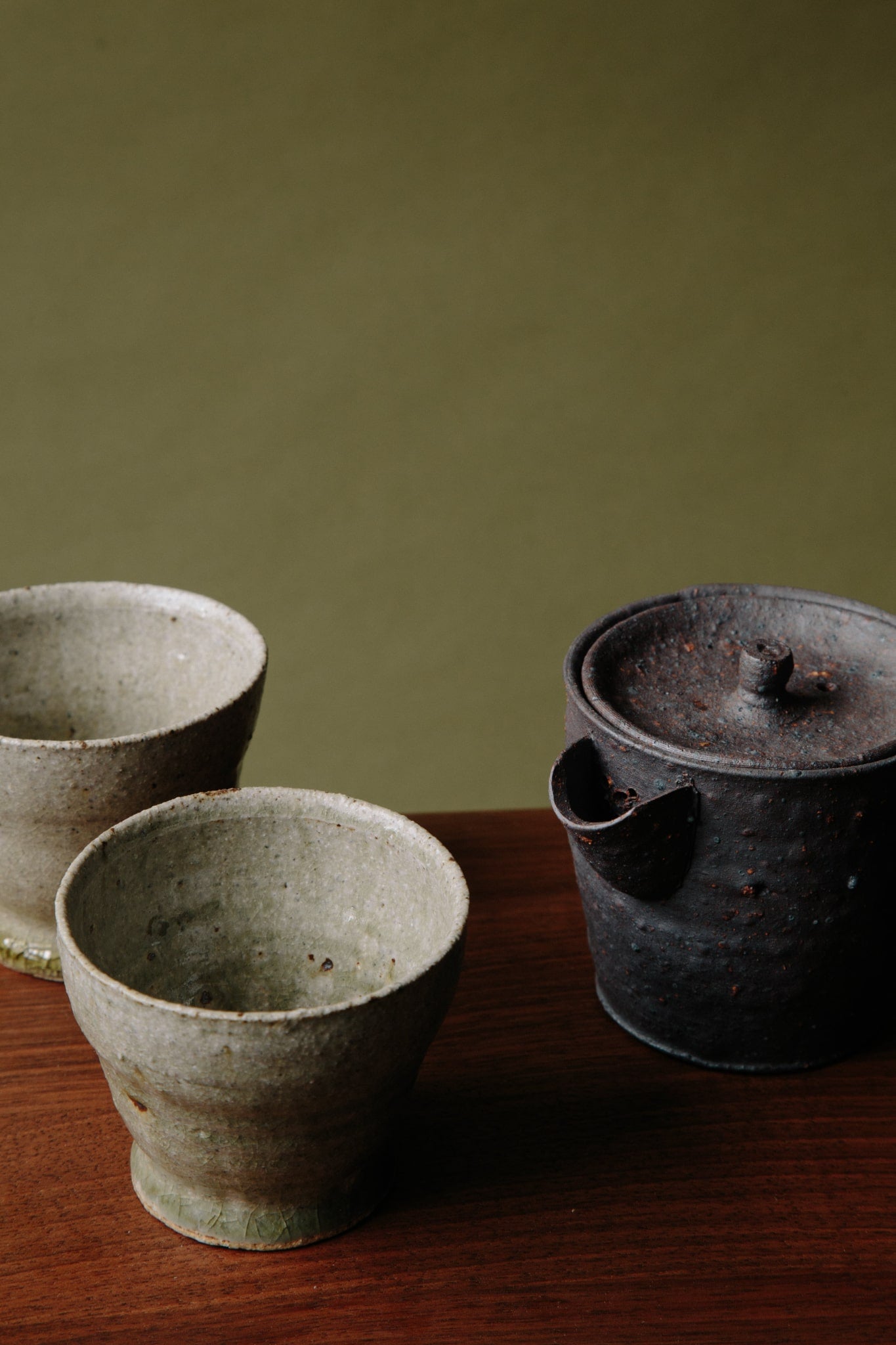 ALT=The small black teapot photographed with two ceramic cups with feet, also by Jonathan Wade. 