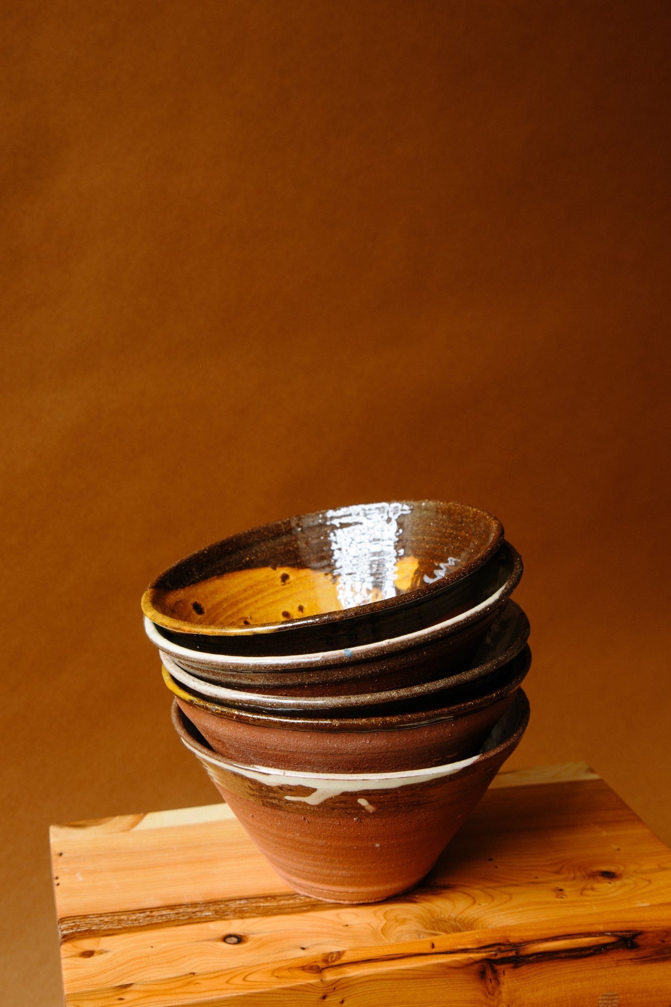 ALT=A stack of five terracotta bowls on a wooden creepie stool from Shetland. The glossy finish on the bowls is relected by the natural light.