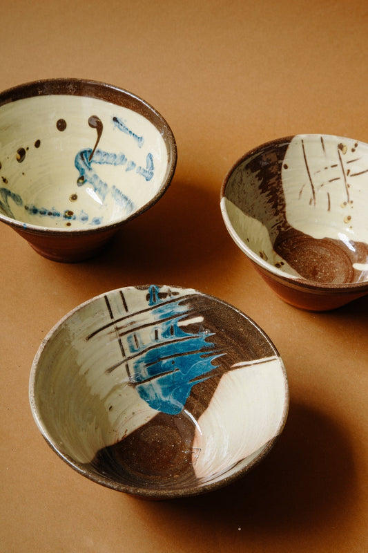 ALT=Three unique terracotta bowls. Mainly white and brown in colour, but with additions of deep blue and expressive painterly marks and scratches. 