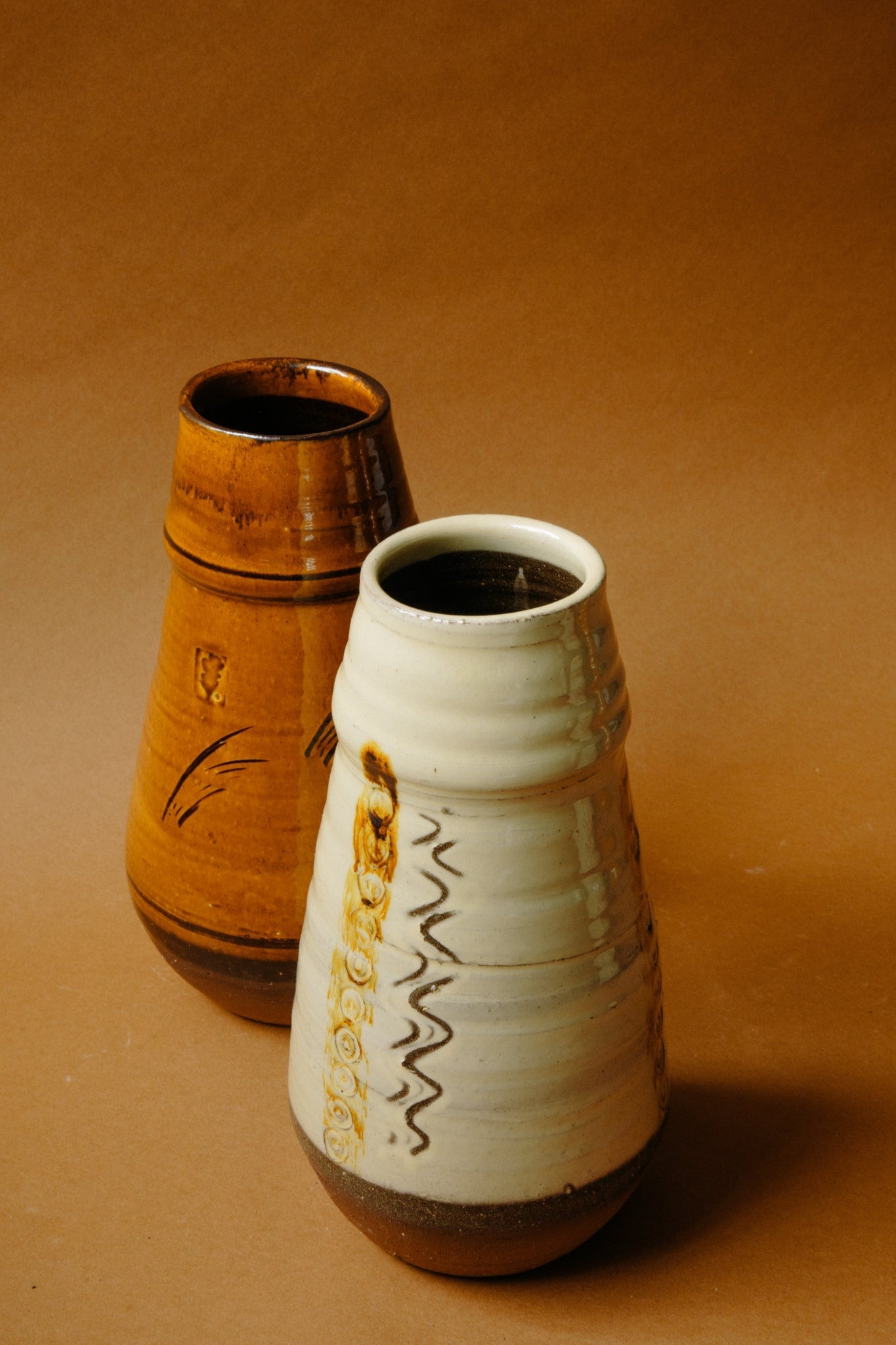 ALT=Large ceramic vases in caramel and white with unique markings. Shot empty on a brown backdrop.