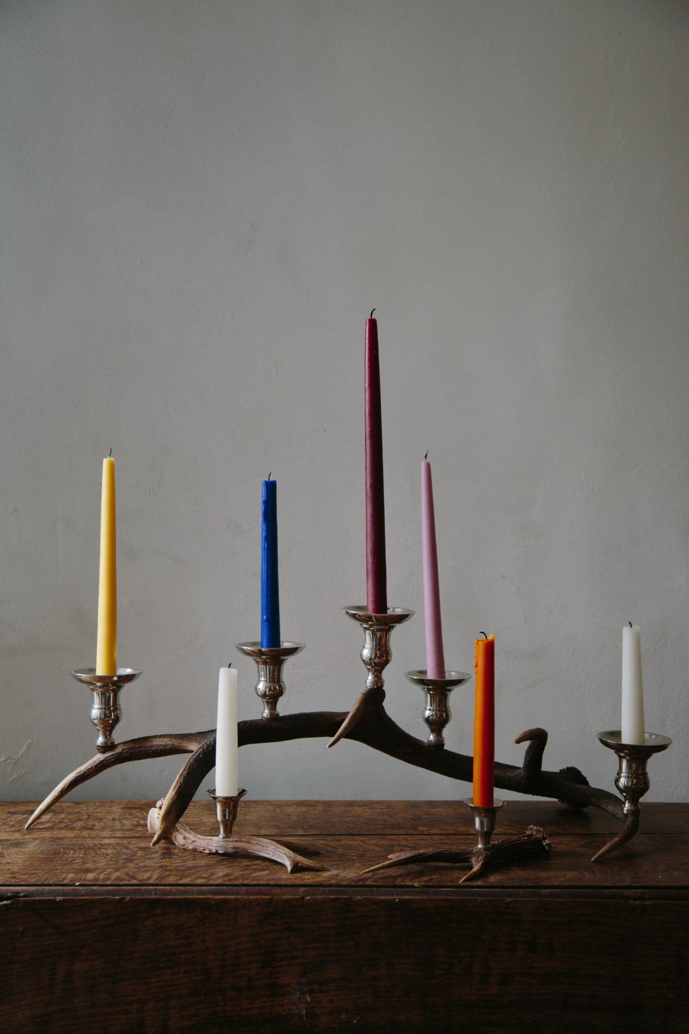 ALT=A display of candlesticks and candelabras on a wooden table top. Styled with colourful candles.