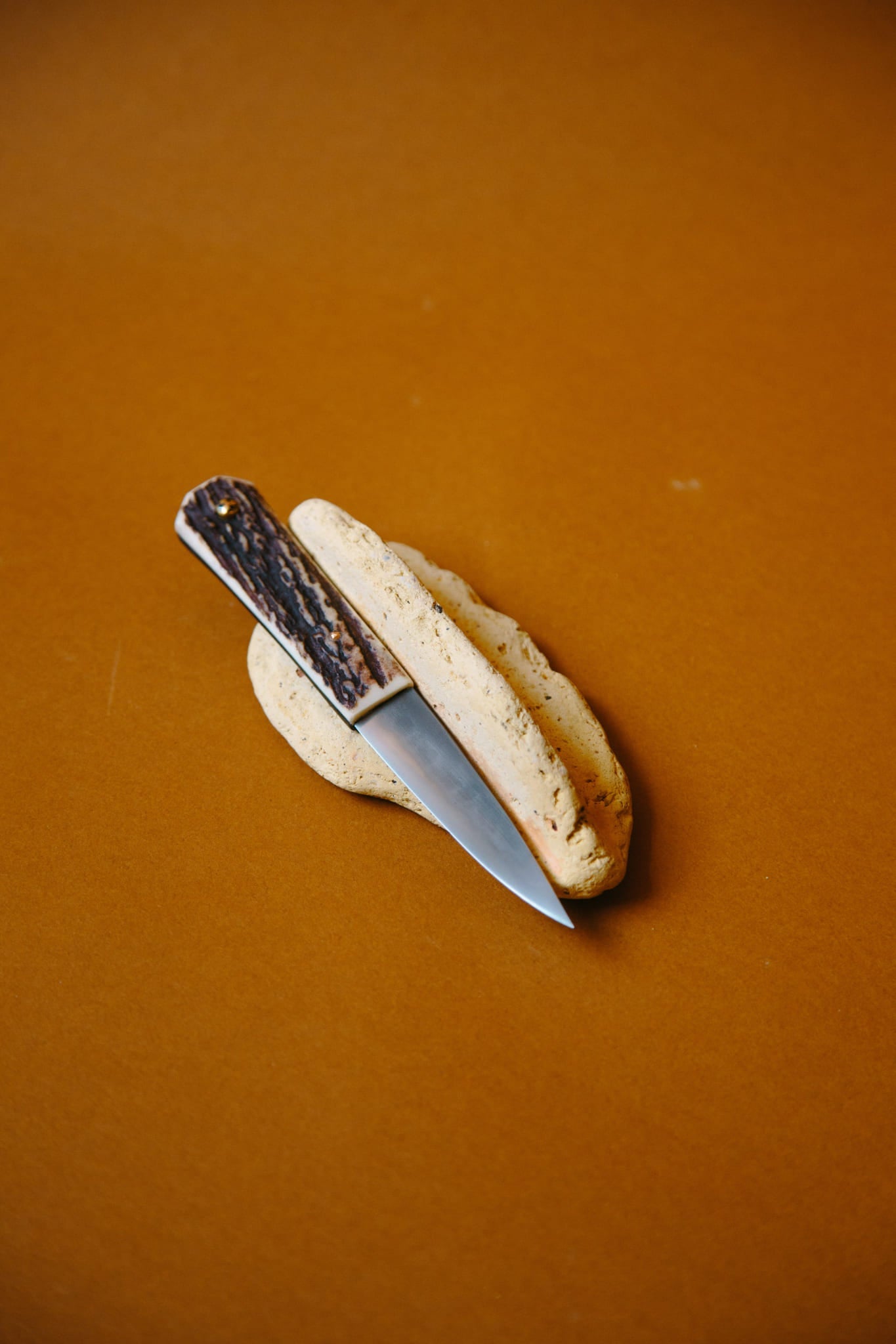 ALT=A traditional Celtic Sgian Dubh knife shown placed on a rock. The handle made from Bog Antler. Shot on a deep brown background.
