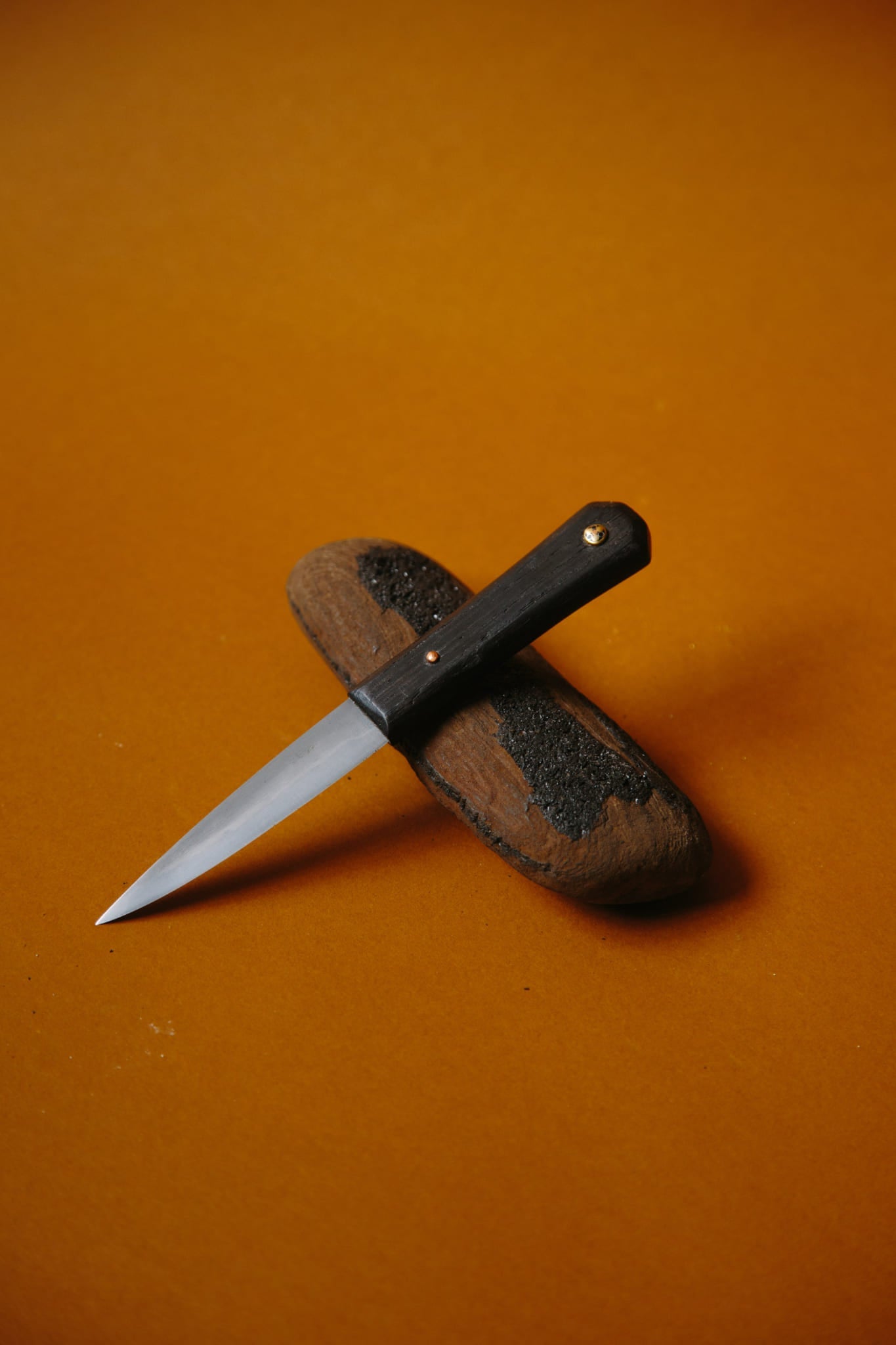 ALT=A traditional Celtic Sgian Dubh knife shown placed on a rock. The handle made from Bog Oak. Shot on a deep brown background.